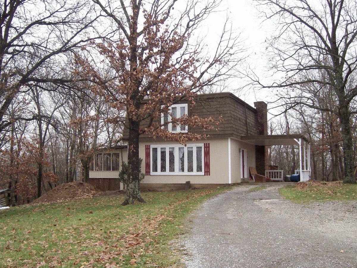 The house at purchase, seen from the driveway: a flat roof over shingled second-story walls, a screened porch at the left and a carport at the right.