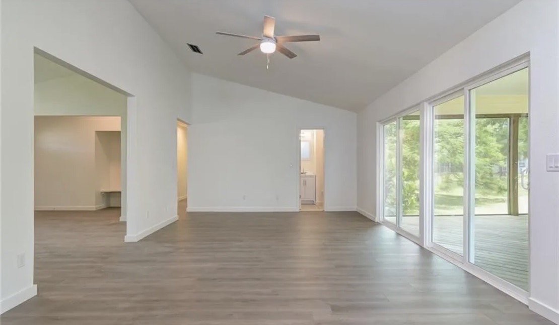 The completed living area under a vaulted ceiling, new plank flooring throughout, sliding doors opening onto the retained screened porch.