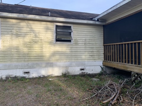 An exterior wall at ground level: siding discolored and deteriorating where it meets the white block stem wall, with two foundation vents below.