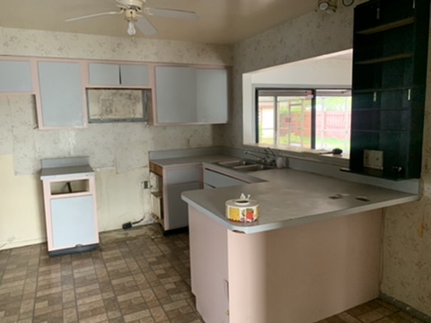 The kitchen at purchase: pink and gray laminate cabinet doors, laminate counters over a peninsula, and dated patterned flooring.